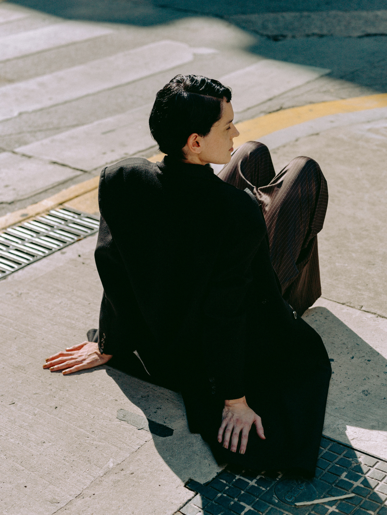 A lone figure in a tailored coat seated on the pavement, seen from behind