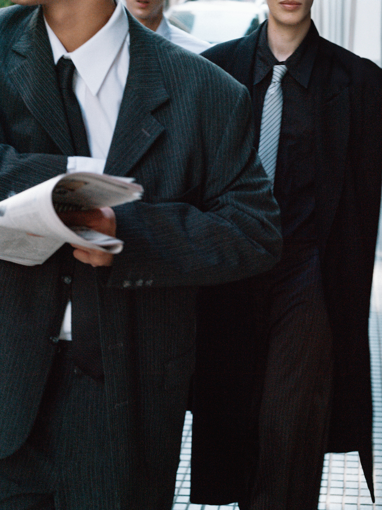 Three professionals in tailored suits, one holding folded newspapers